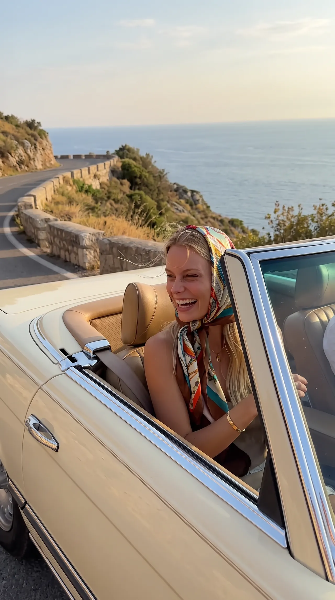 Sofia laughing in a convertible on a coast road